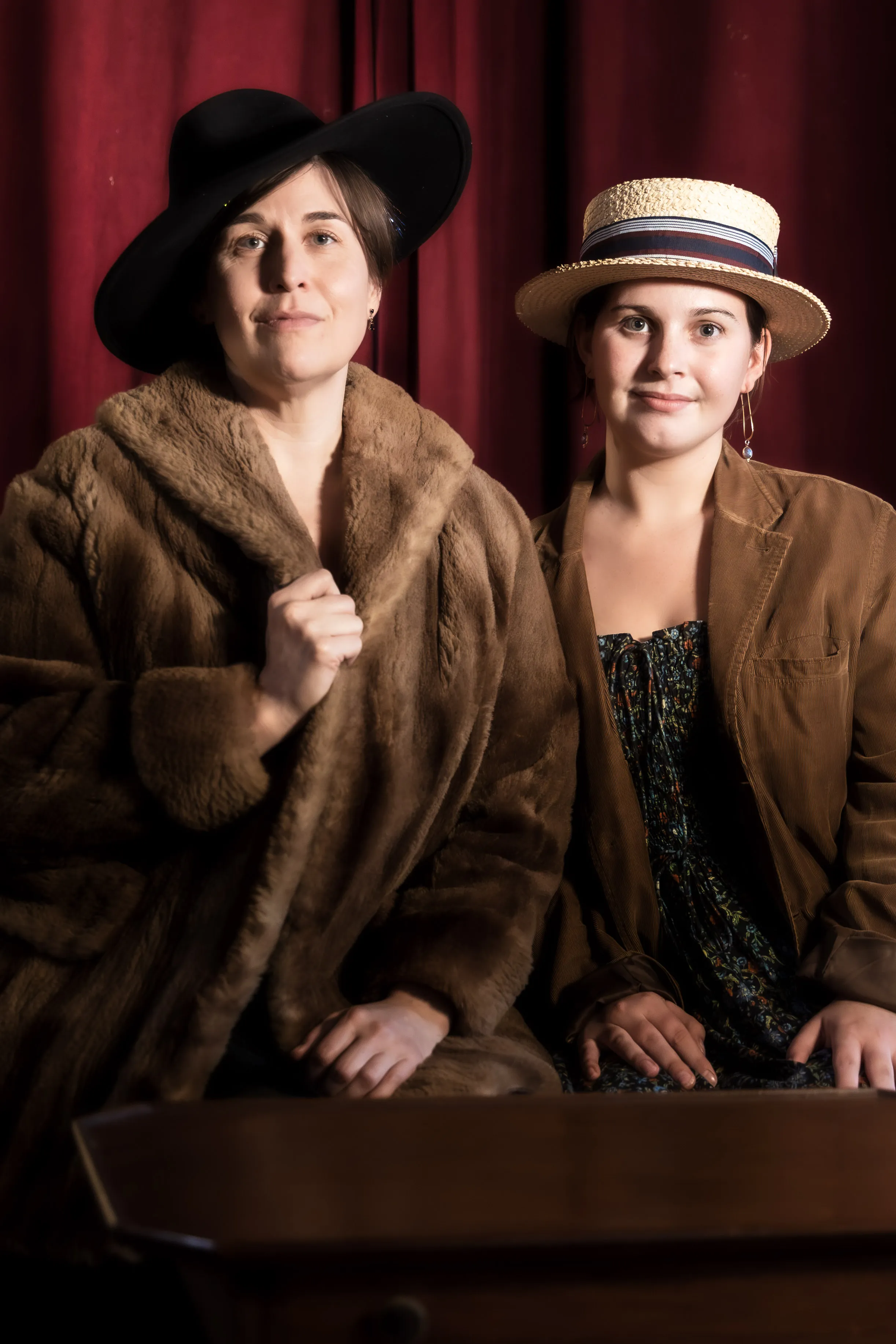 Two costumed performers sit together, wearing a fur coat and a straw boater hat.