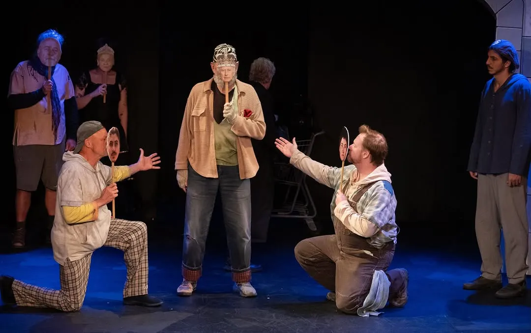 An ensemble scene with one performer kneeling and another gesturing towards the group.