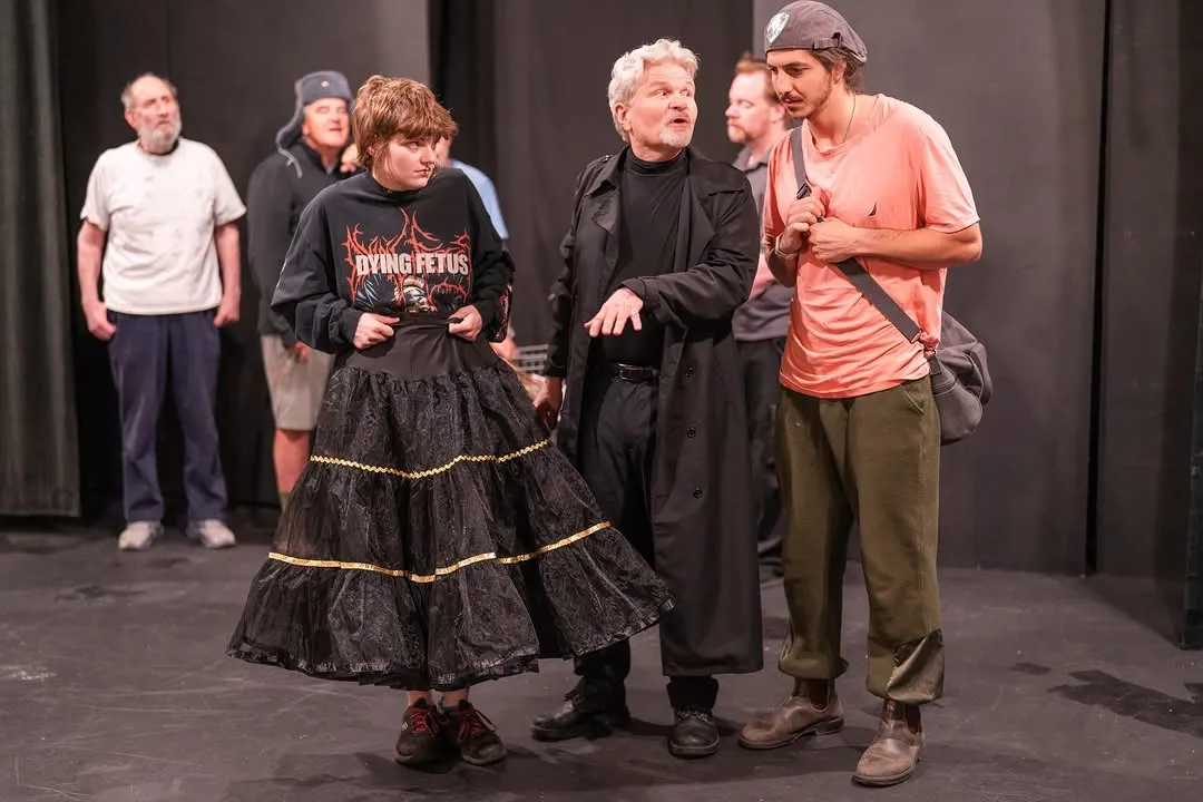 Cast rehearsing a scene, including a performer in a long black costume.