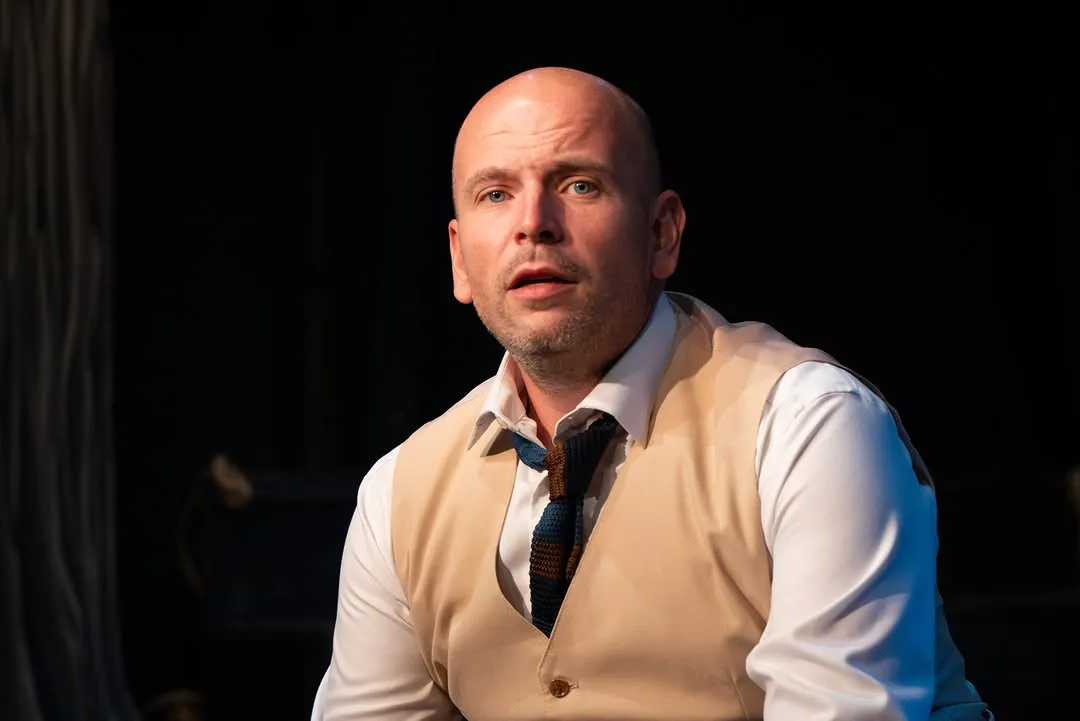 A performer on stage wearing a pale shirt and blue neck cloth.