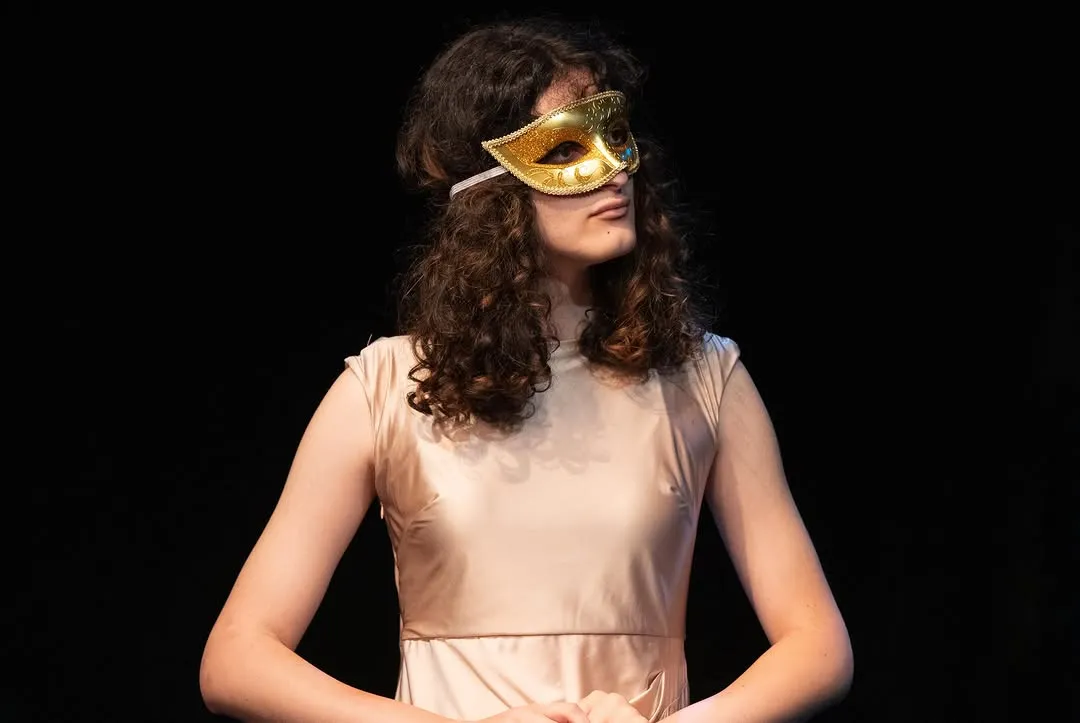 A performer wearing a black dress and a gold mask.
