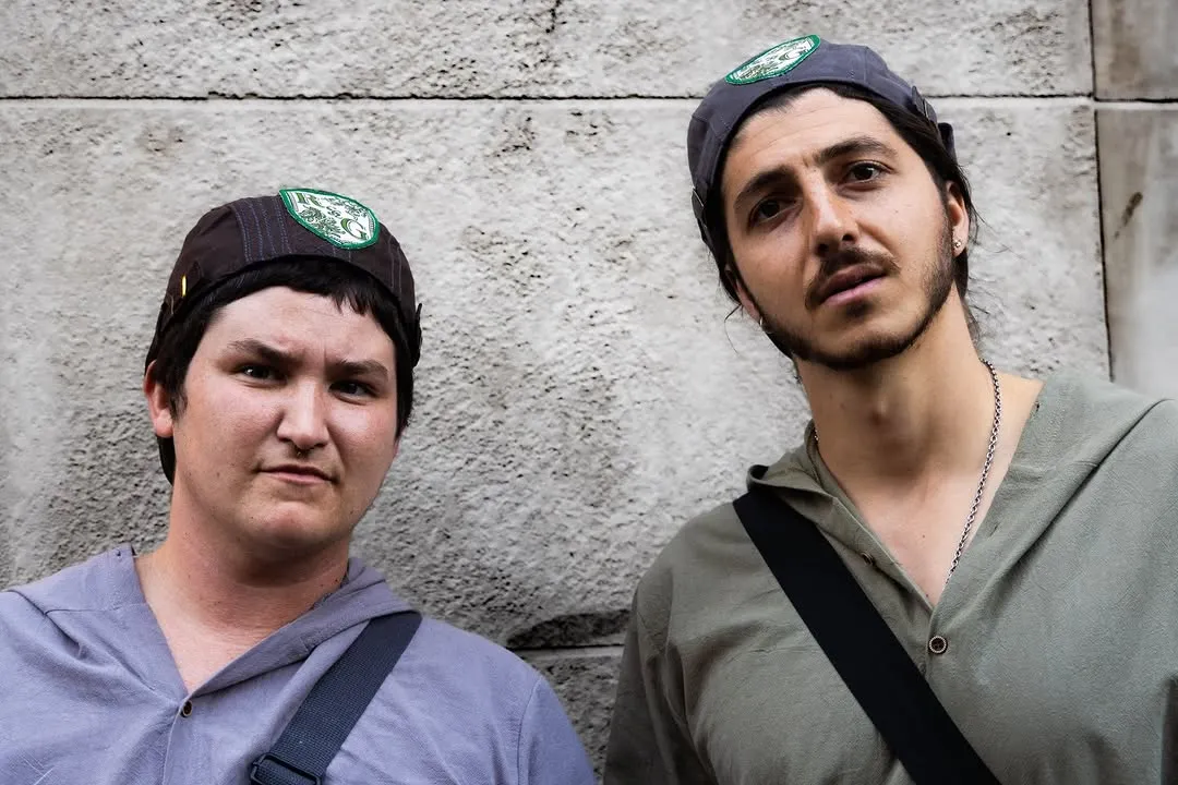 Rosencrantz and Guildenstern posed against a stone wall.