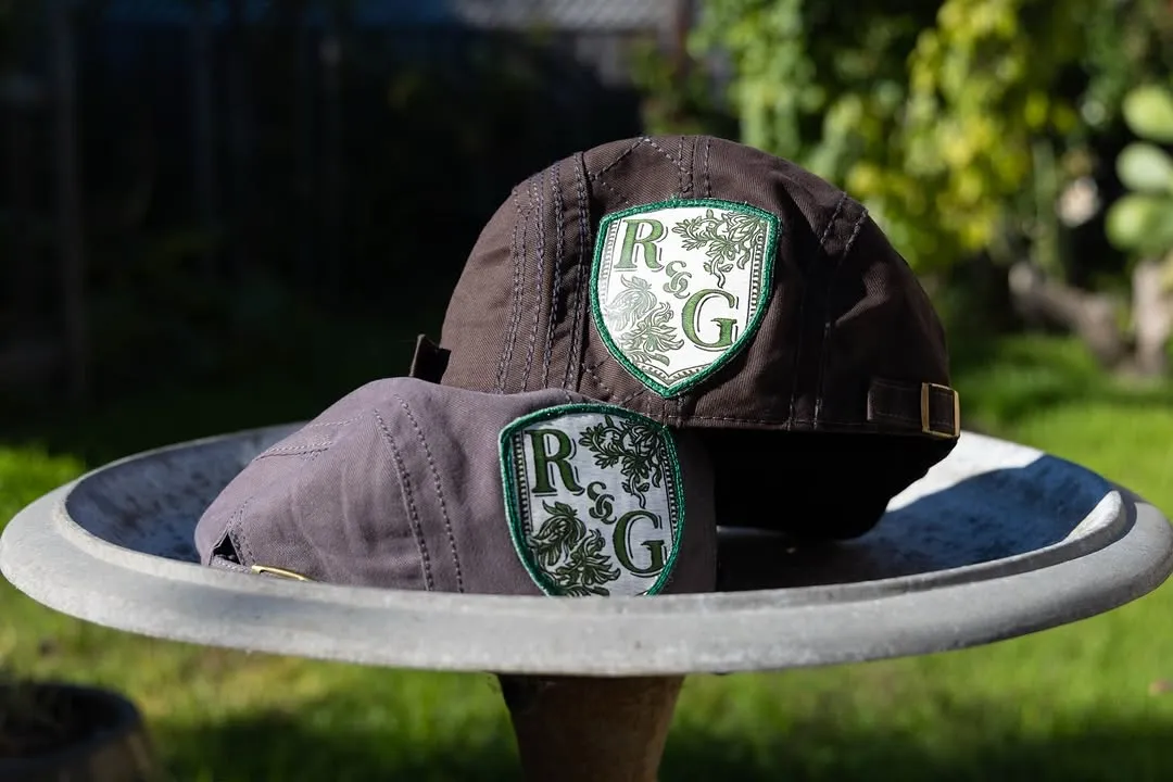 Two caps bearing R&G emblems resting together in a garden.