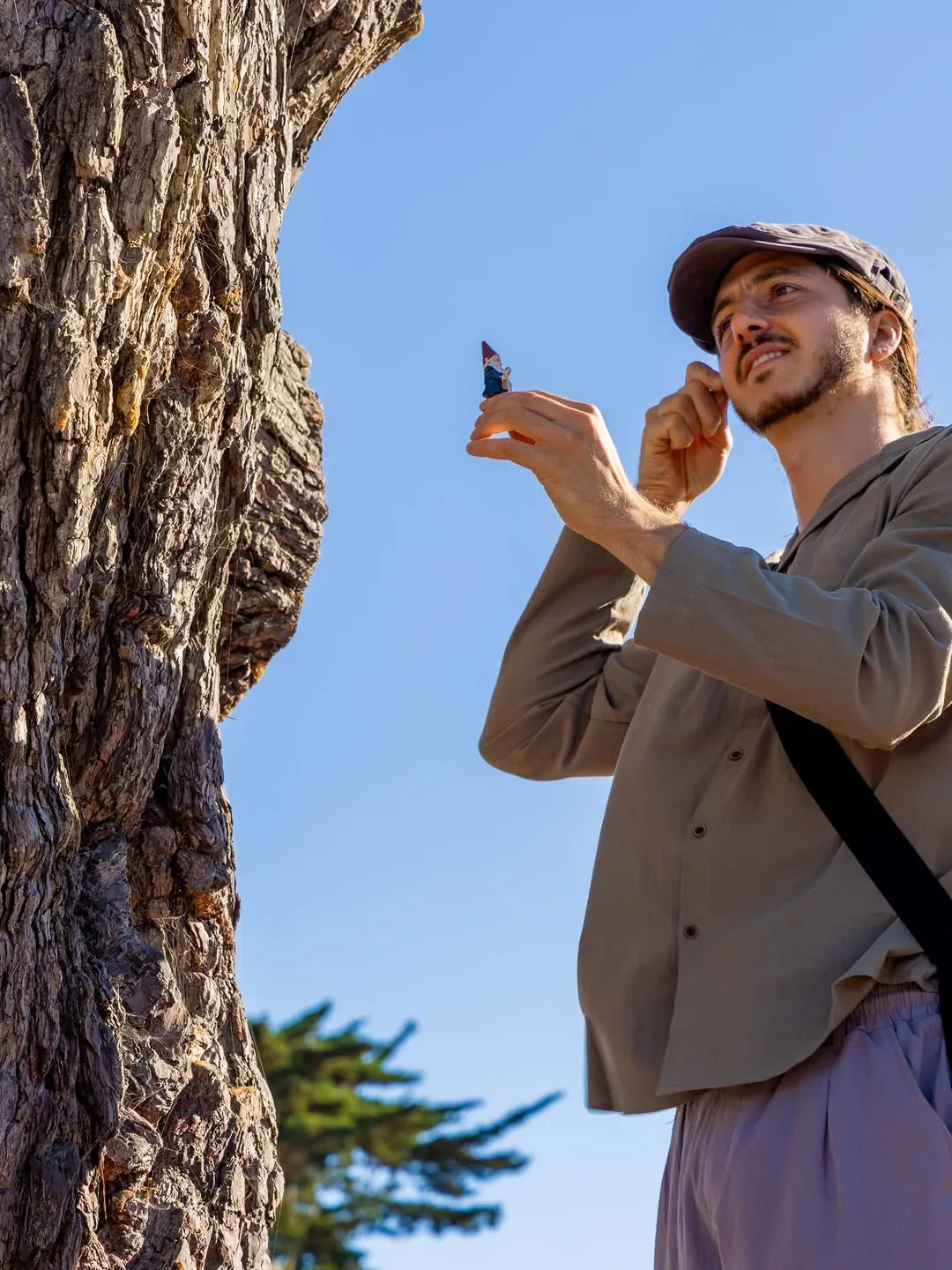 A costumed performer leaning against a tree and gesturing with one hand.