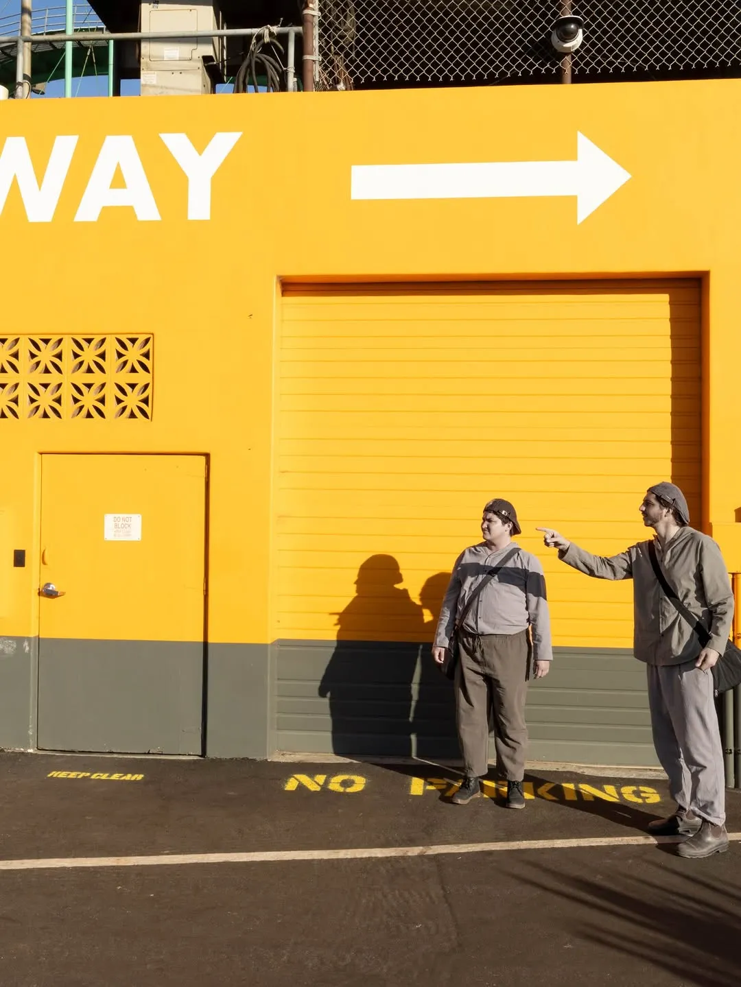 Two costumed performers beneath a large arrow on a yellow wall.