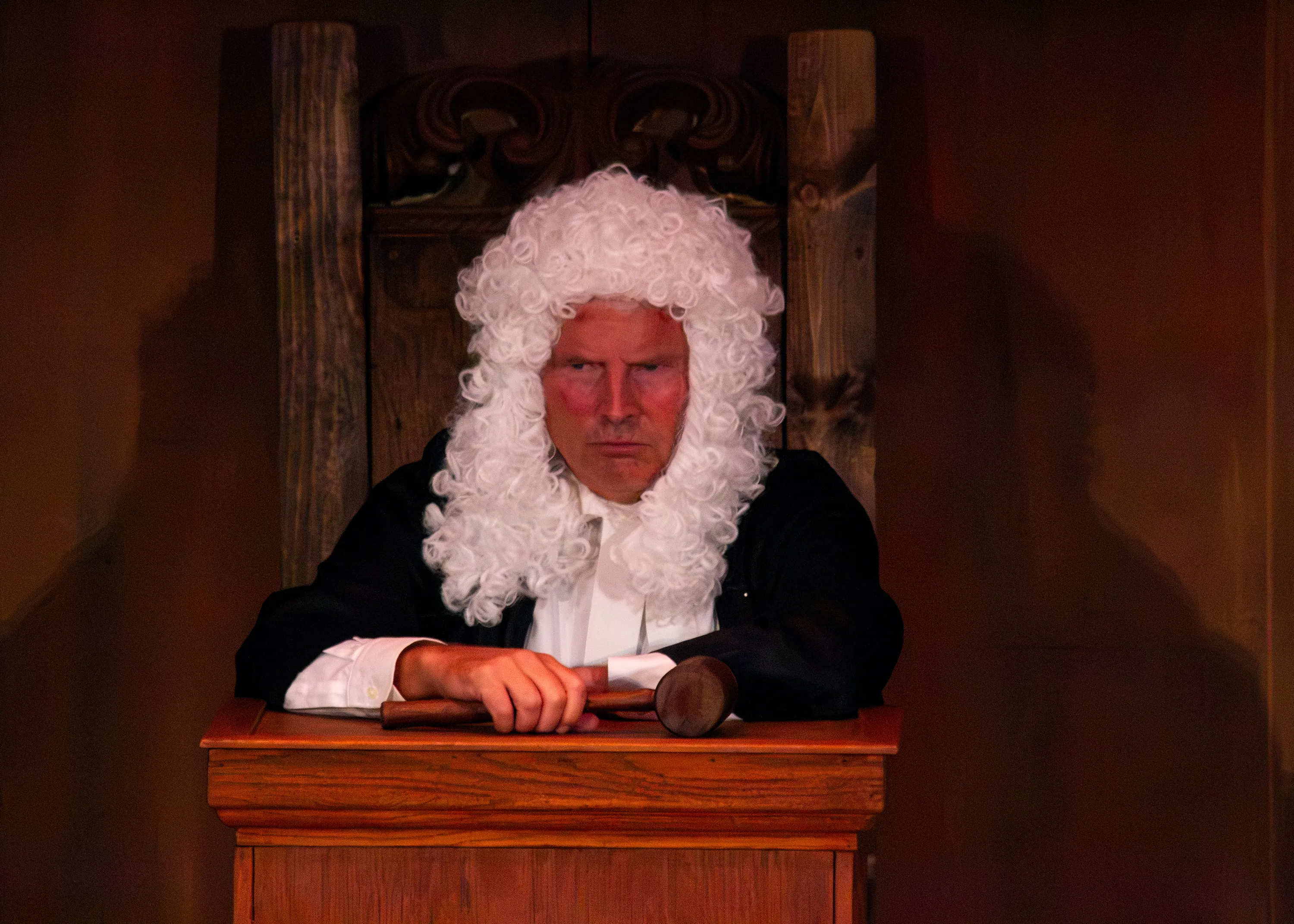 A judge in a white wig sits behind the wooden courtroom bench.